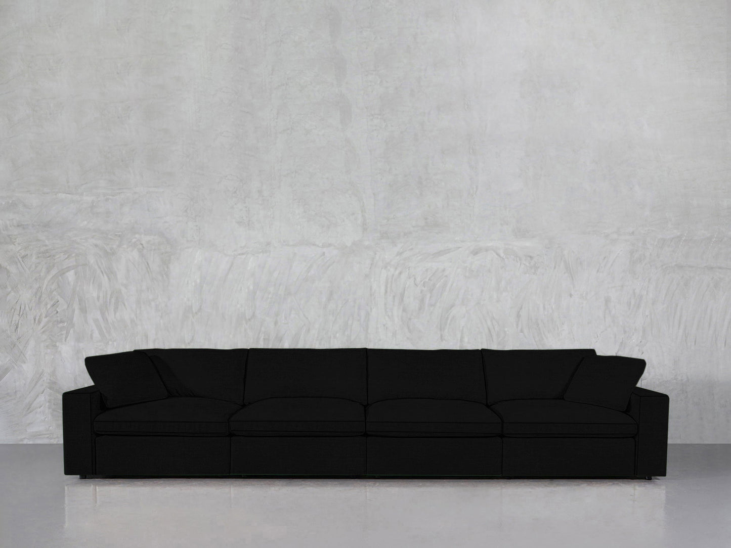 A 4-Seat Modular Sofa in black with four seat cushions is placed against a plain, light gray textured wall on a shiny, light-colored floor.