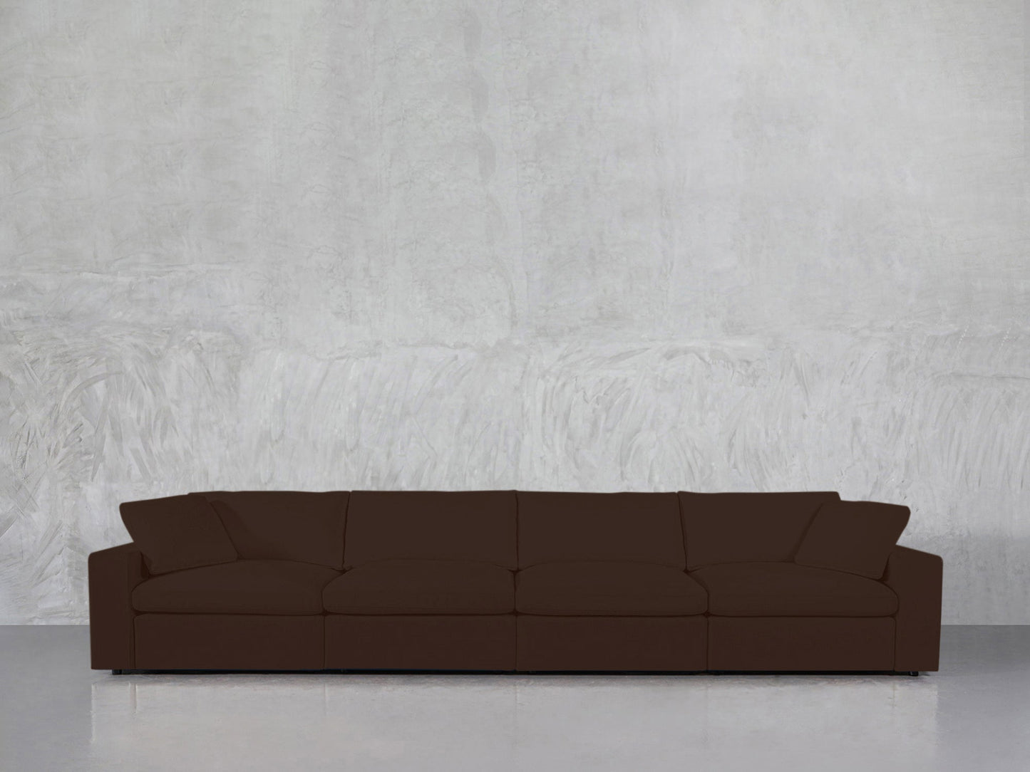 The 4-Seat Modular Sofa, in dark brown with wide armrests, is placed against a light gray textured wall on a shiny, light-colored floor.