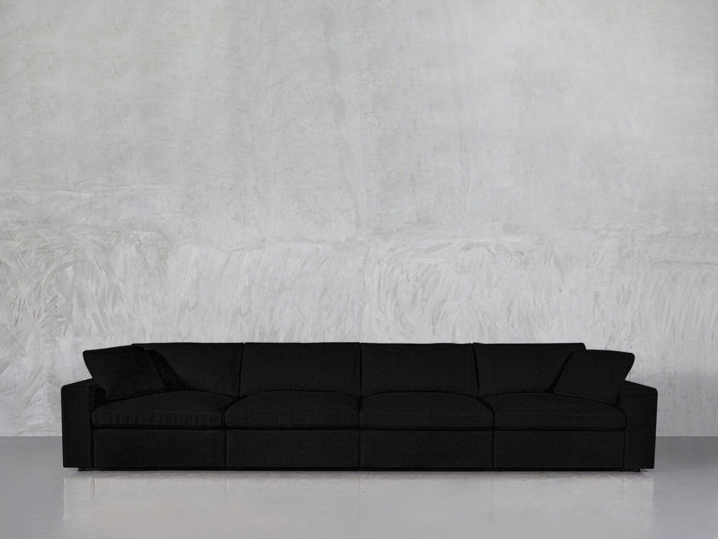 A 4-Seat Modular Sofa in black with a modern design sits against a light gray textured wall on a shiny, reflective floor in a minimalist setting.