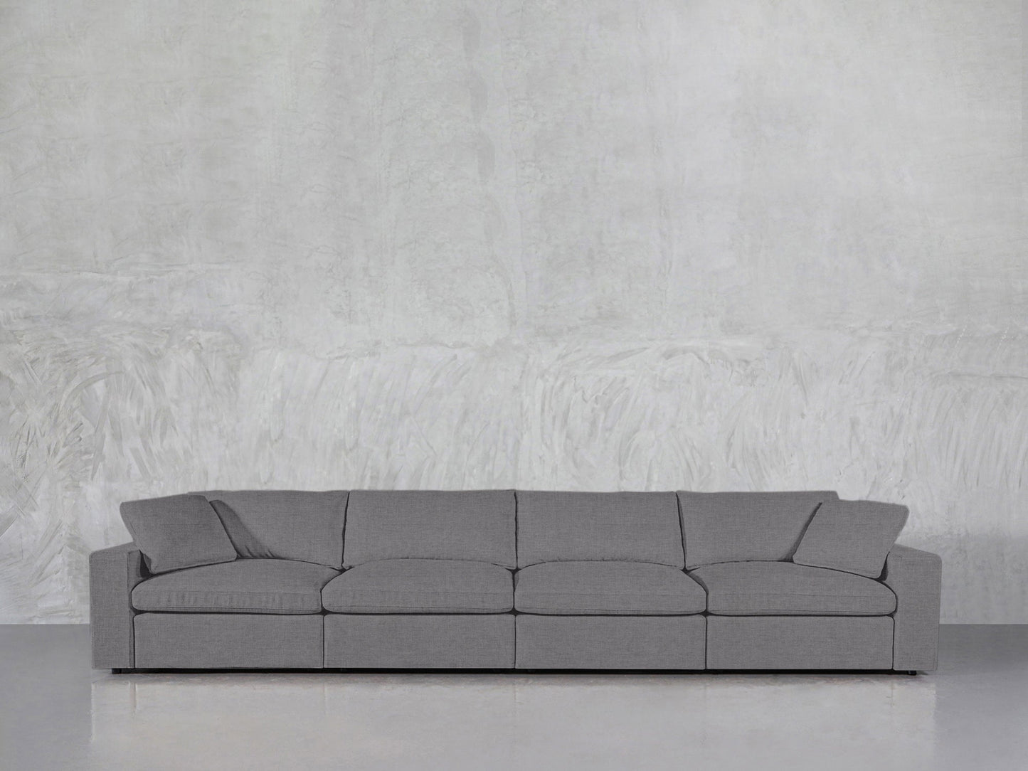 The 4-Seat Modular Sofa, featuring a modern minimalist design with four seat cushions and two armrests, is positioned against a light grey textured wall on a polished floor.