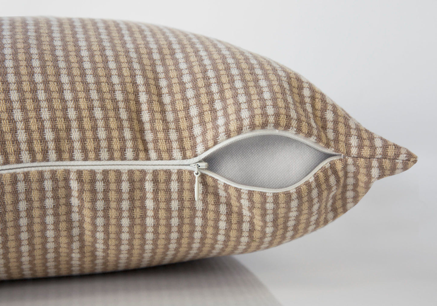 A close-up of a brown and beige checkered decorative throw pillow (square, insert included, hypoallergenic) with a white zipper partially open, showing the white inner lining. The background is plain and light-colored.