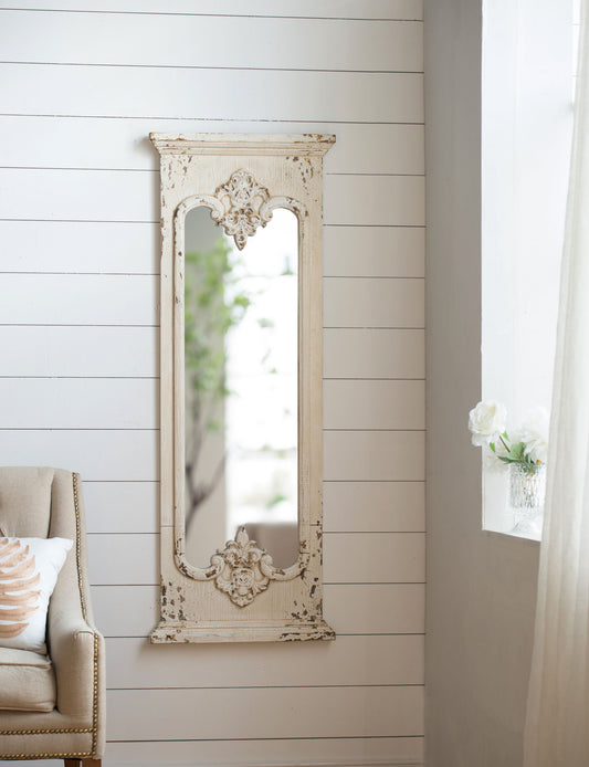 The Full Length Mirror With Solid Wood Frame in white hangs on a shiplap wall near a window with sheer curtains. A beige armchair and a vase of white flowers sit nearby, creating an elegant entryway or living room setting.