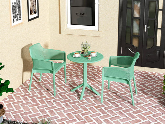 A cozy patio displays the 3 Piece Plastic Arm Chair Bistro Grs Premium Ocean Plastic set in mint green, with coffee cups, flowers, and a plate, arranged on a red-and-white herringbone brick floor by beige walls and black doors.