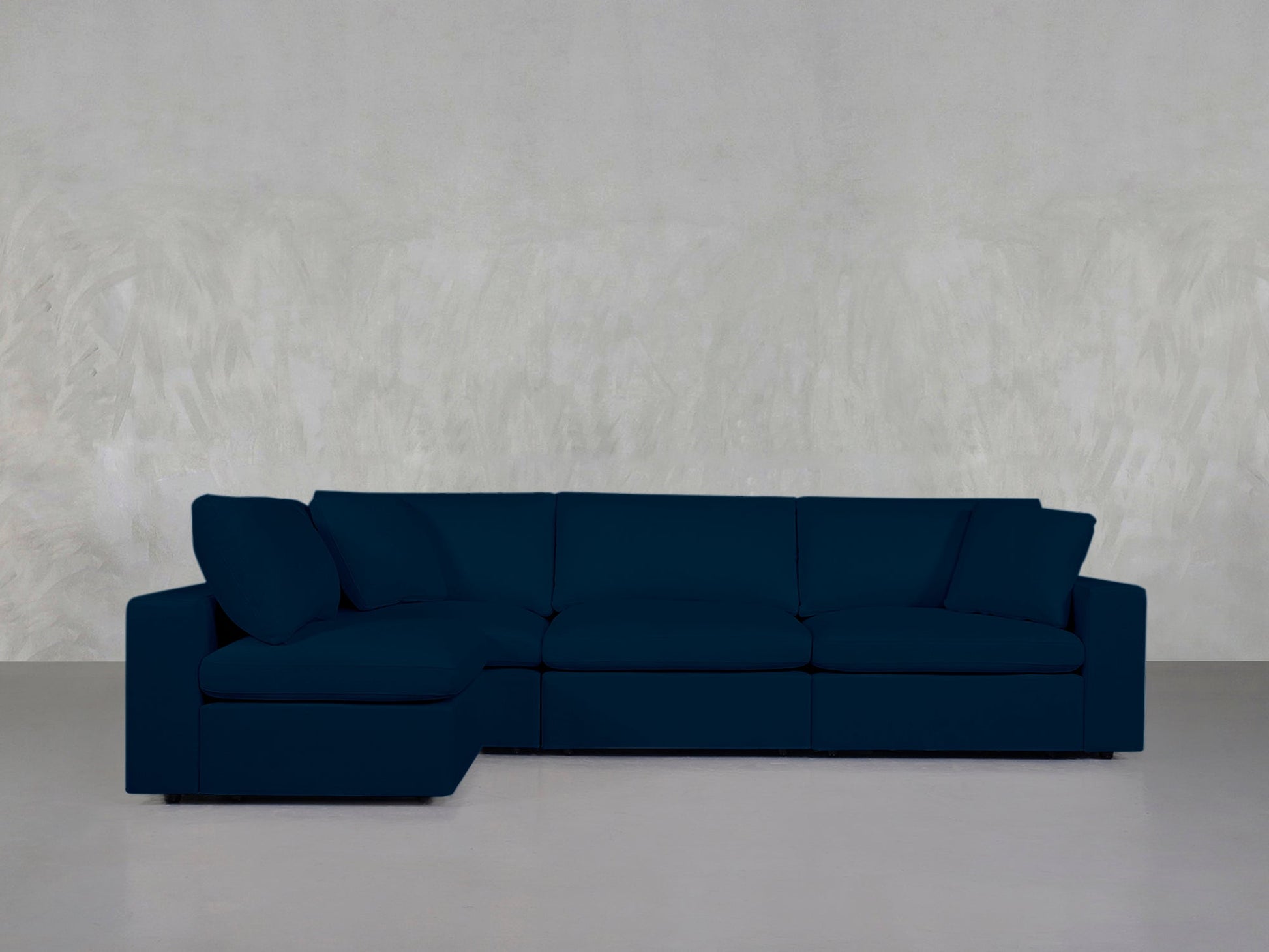 The 4-Seat Modular Open Corner Sectional in deep blue with clean lines and a left-facing chaise stands against a light gray textured wall and a smooth, light-colored floor.