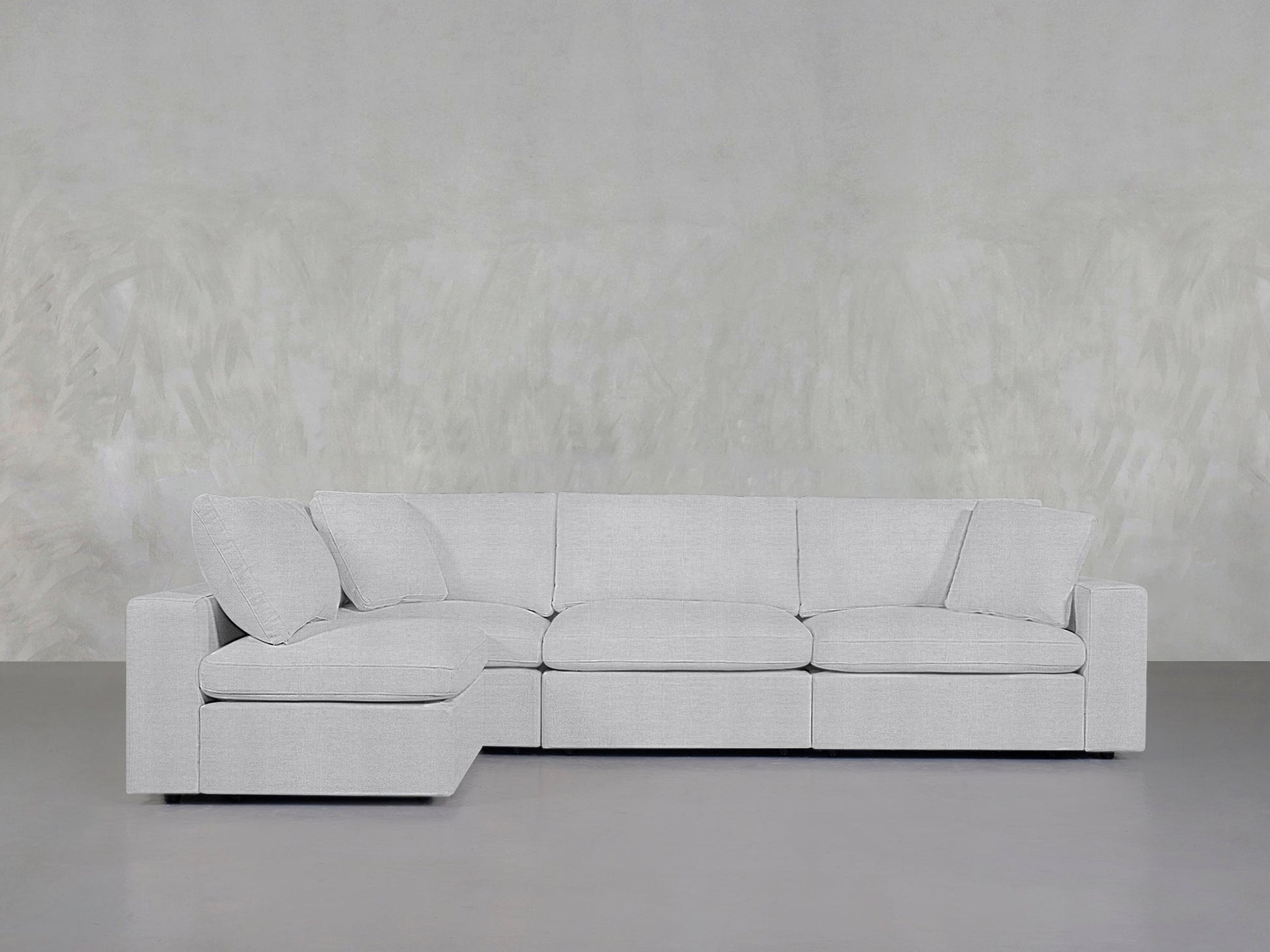The 4-Seat Modular Open Corner Sectional with clean lines and plush cushions sits against a textured light gray wall in a minimalistic room.