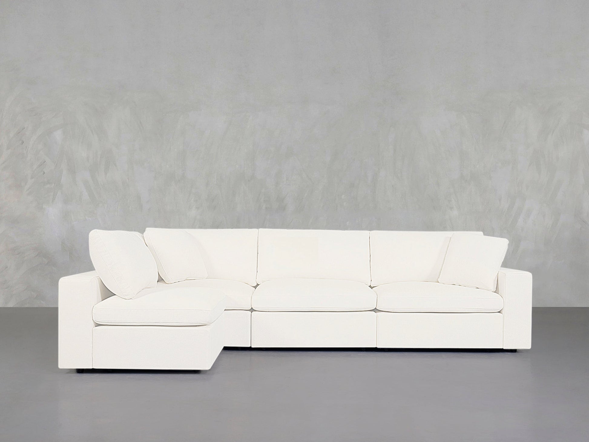 The 4-Seat Modular Open Corner Sectional, featuring a modern white design with clean lines and plush cushions, is placed against a plain light gray textured wall and gray floor.