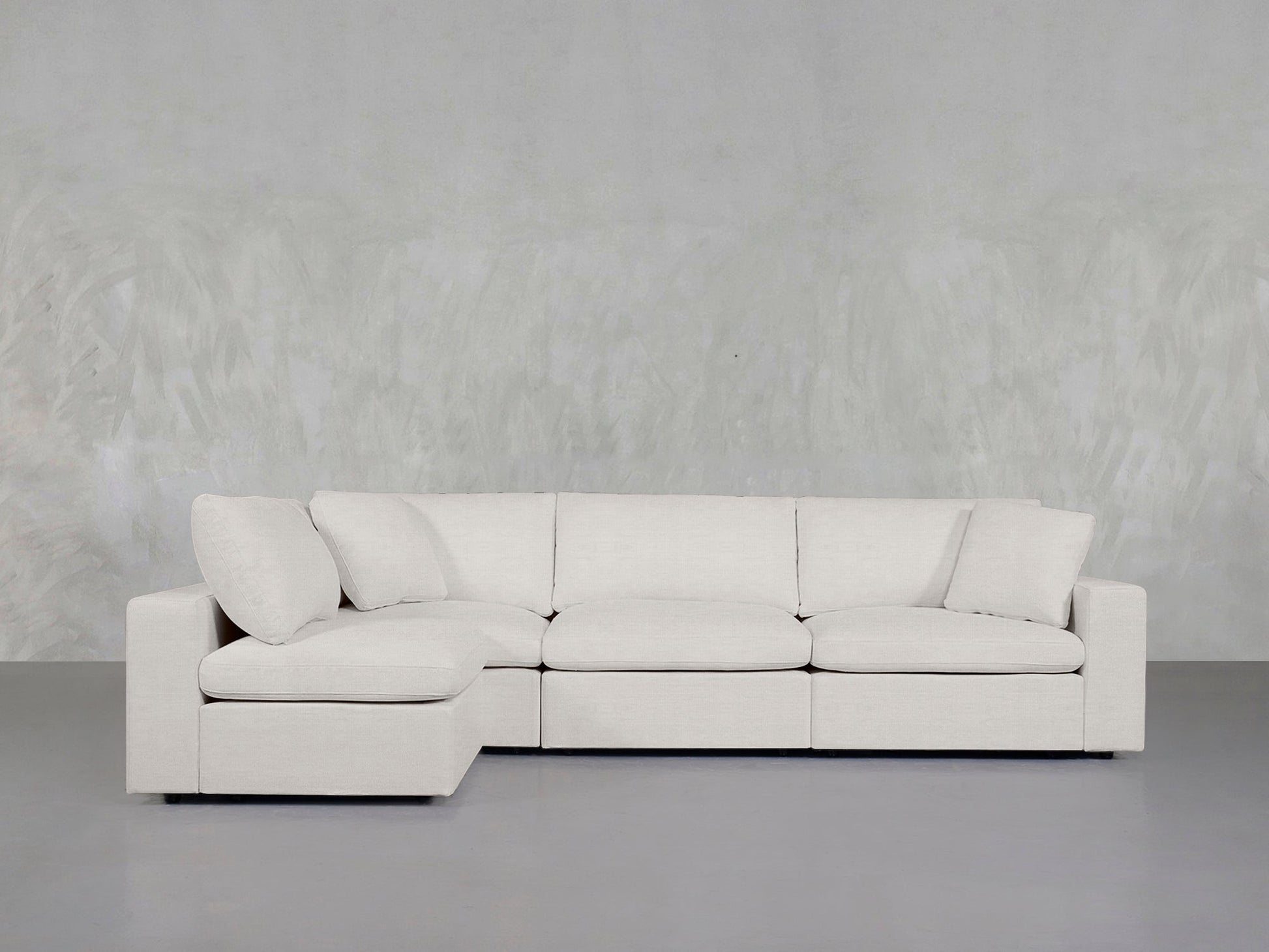 The 4-Seat Modular Open Corner Sectional, featuring plush cushions and clean lines in light beige, sits against a textured pale gray wall on a smooth gray floor.