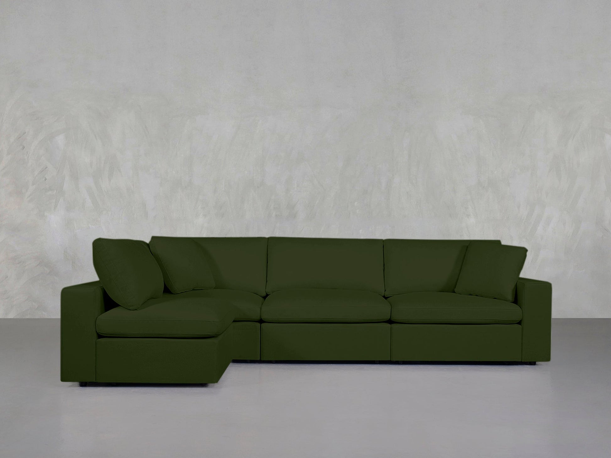 A modern 4-Seat Modular Open Corner Sectional in dark green with a left chaise lounge, set against a light gray textured wall and plain gray floor.