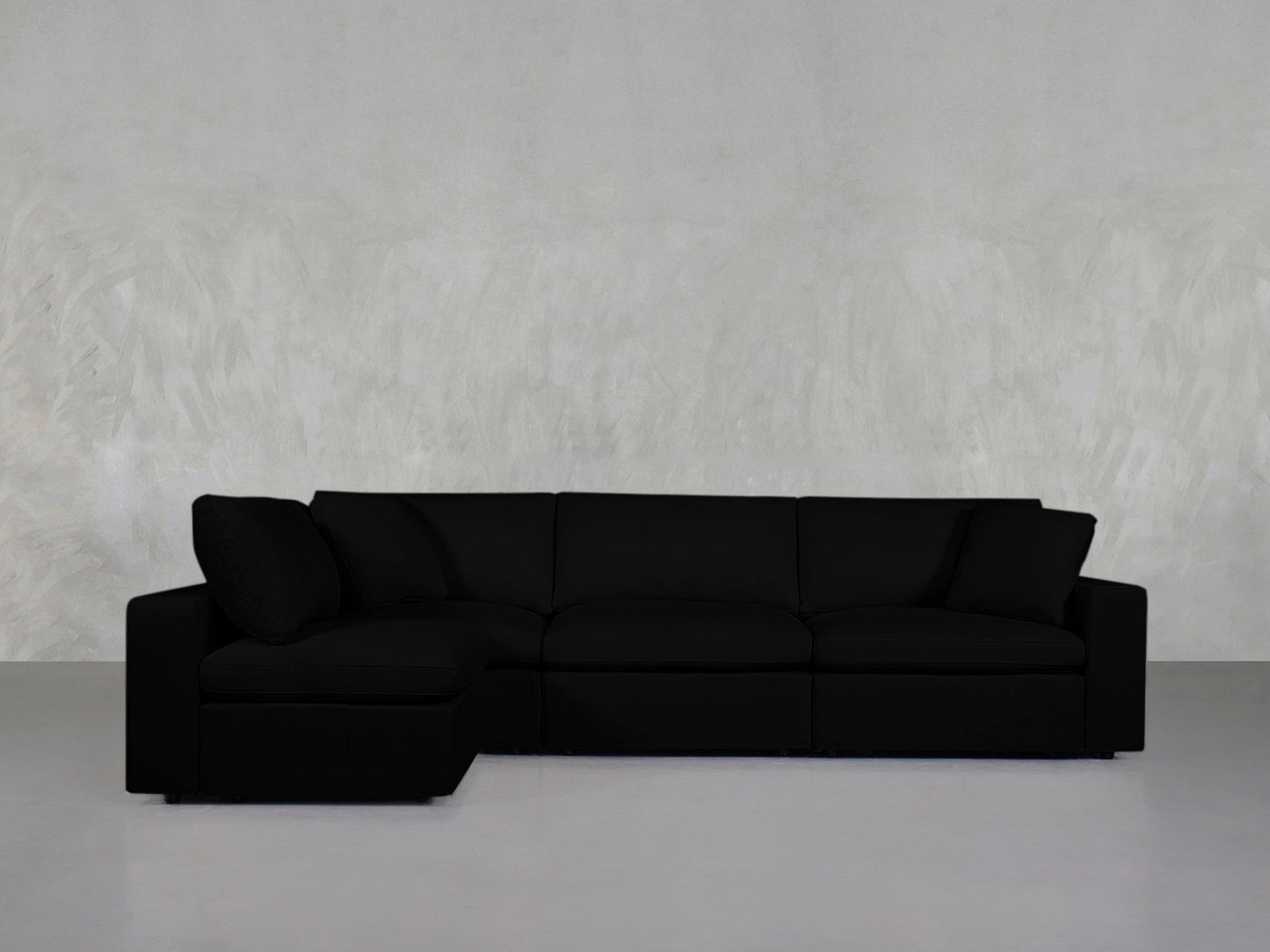 A 4-Seat Modular Open Corner Sectional in black with a left-side chaise is placed against a light gray textured wall and a smooth gray floor.