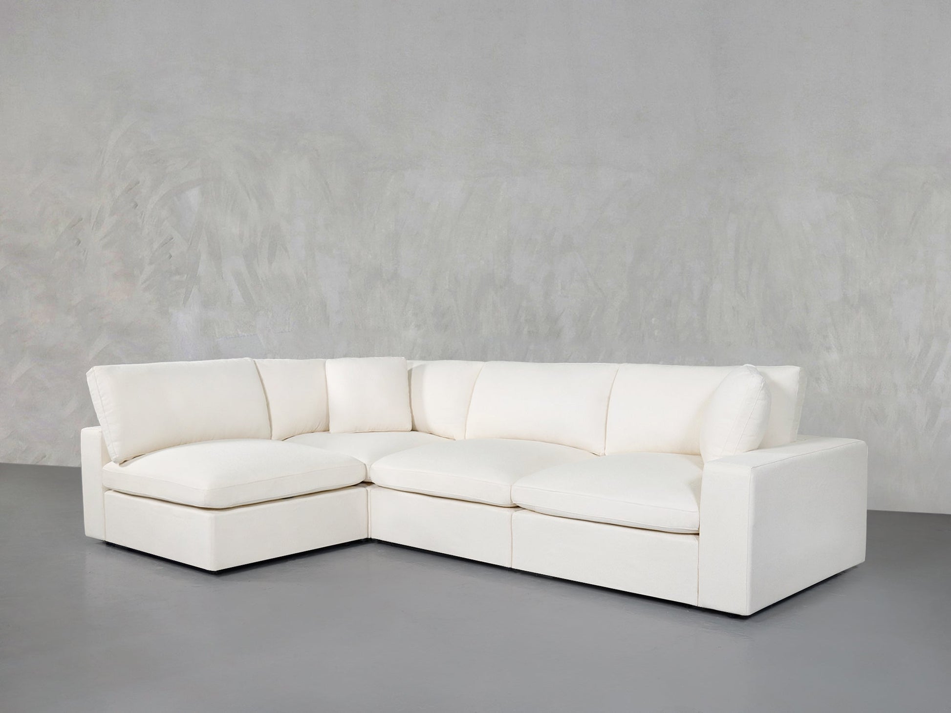 The 4-Seat Modular Open Corner Sectional in white, featuring wide cushions and low armrests, rests on a gray floor against a textured light gray wall.