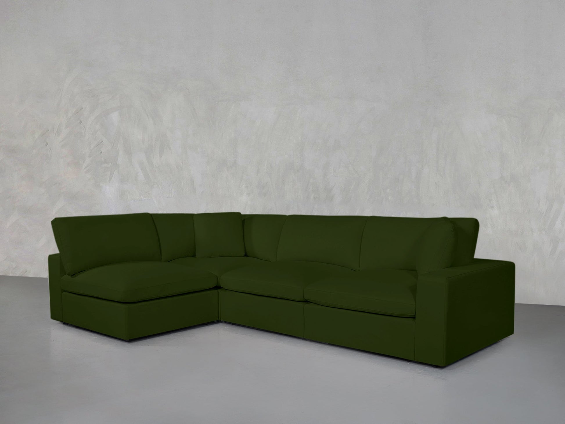 A 4-Seat Modular Open Corner Sectional in dark green is placed in an empty room with light gray walls and a pale gray floor.