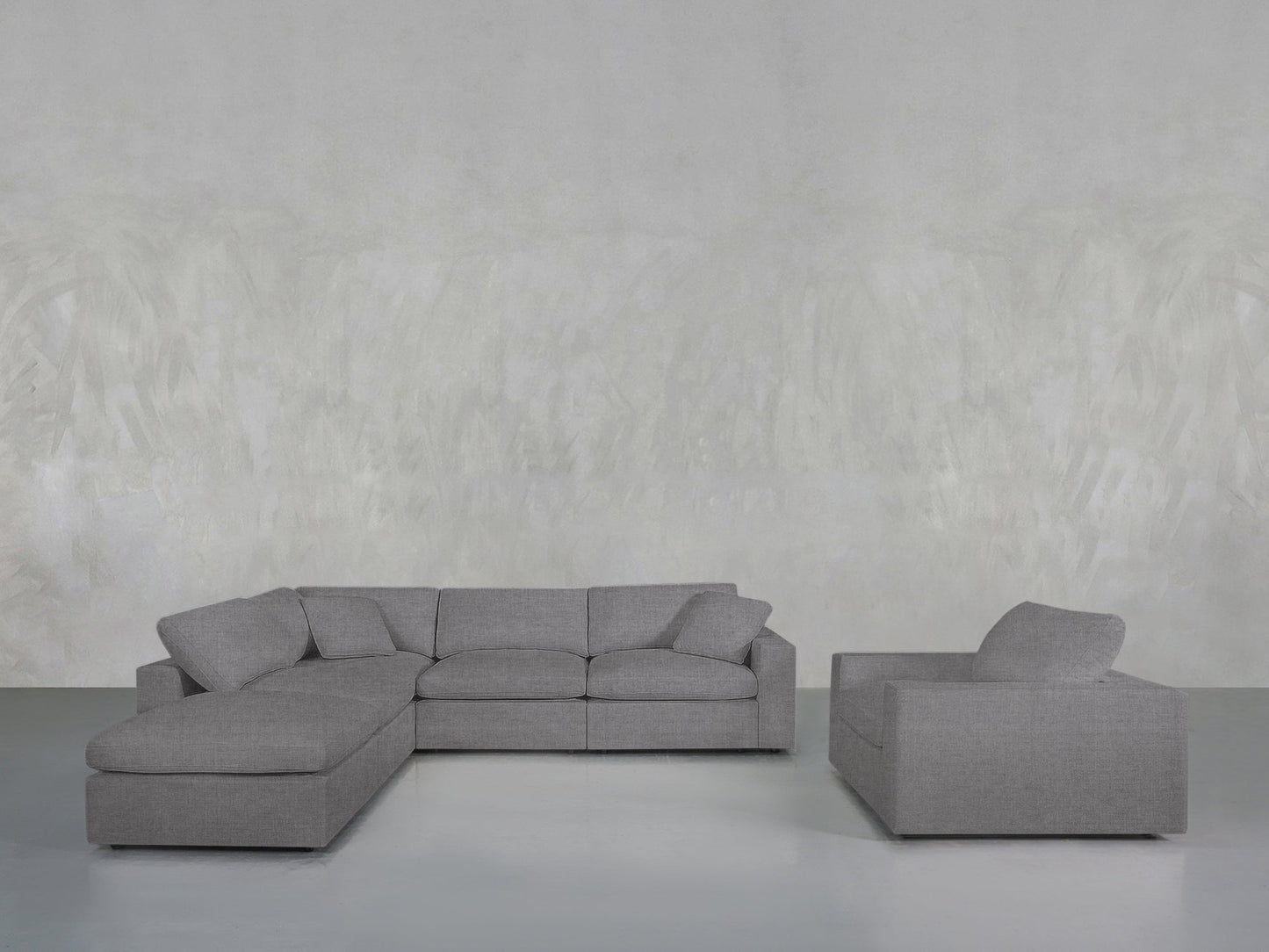 A contemporary living room showcases the 5-1 Sectional & Armchair Set in gray, with a left-side chaise lounge and a matching armchair, both placed against a simple textured gray wall.