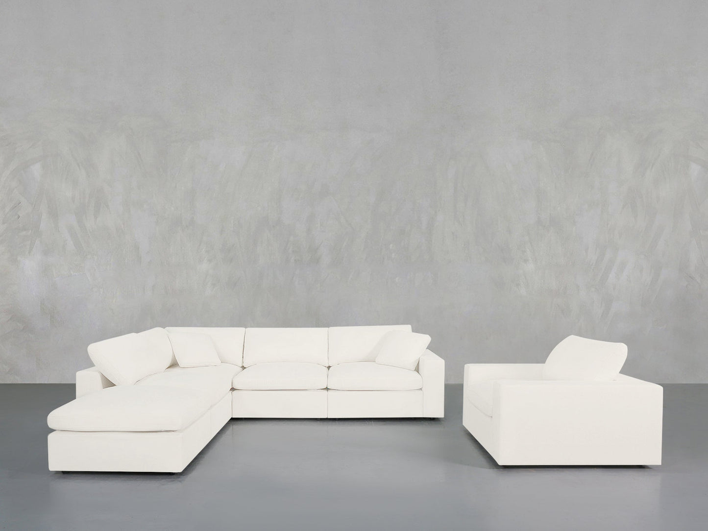 A minimalist room featuring the 5-1 Sectional & Armchair Set in white, positioned against a light gray textured wall and a smooth gray floor.