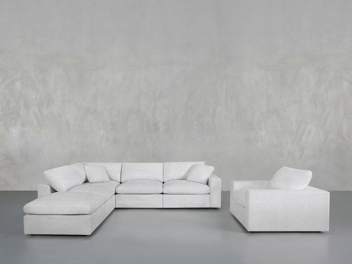 A modern living room features the 5-1 Sectional & Armchair Set in light gray, both with cushions, placed against a plain textured light gray wall and a smooth gray floor.