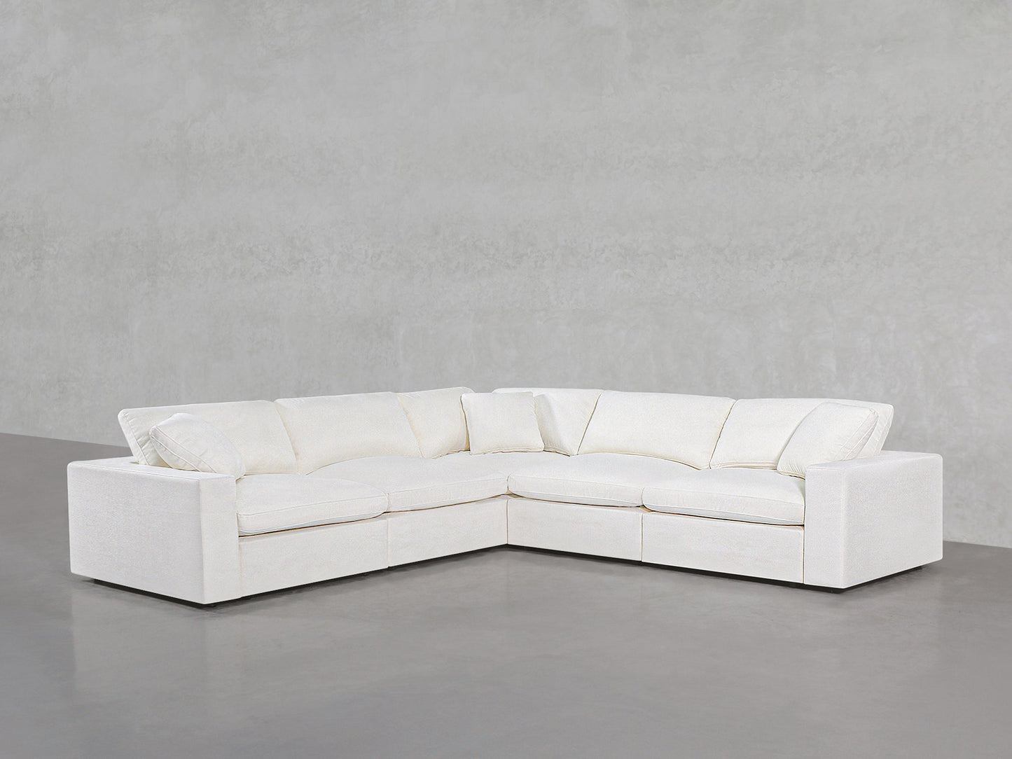 The 5-Seat Modular Corner Sectional, featuring clean lines and plush cushions in modern white, sits on a smooth gray floor against a light gray textured wall.