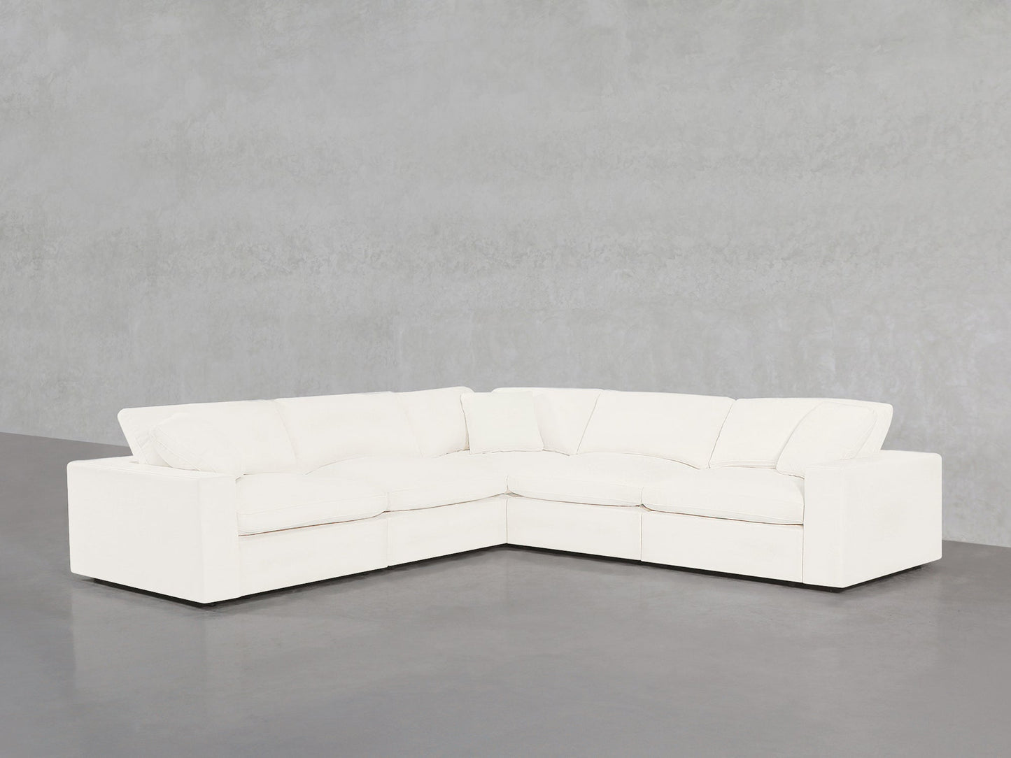 A 5-Seat Modular Corner Sectional with plush cushions is placed on a smooth gray floor against a light gray, textured wall.