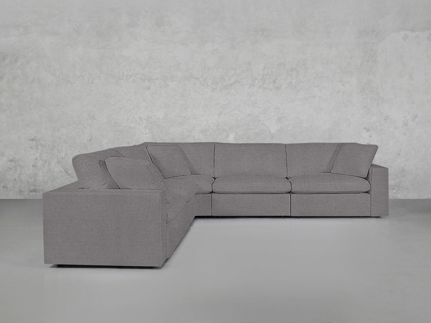 A contemporary 5-Seat Modular Corner Sectional in light gray, featuring three seat and three back cushions, positioned before a plain, light gray textured wall and floor.