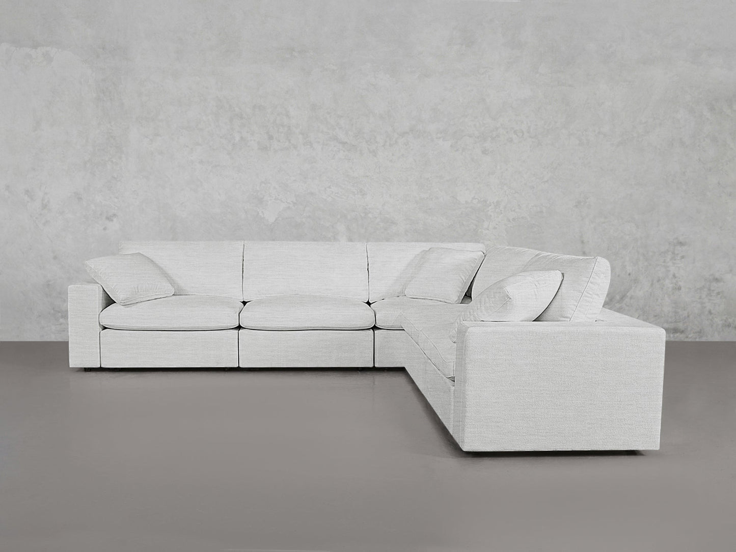 A modern, light gray 5-Seat Modular Corner Sectional with clean lines sits against a textured gray wall and smooth gray floor, featuring four matching cushions on the sofa.