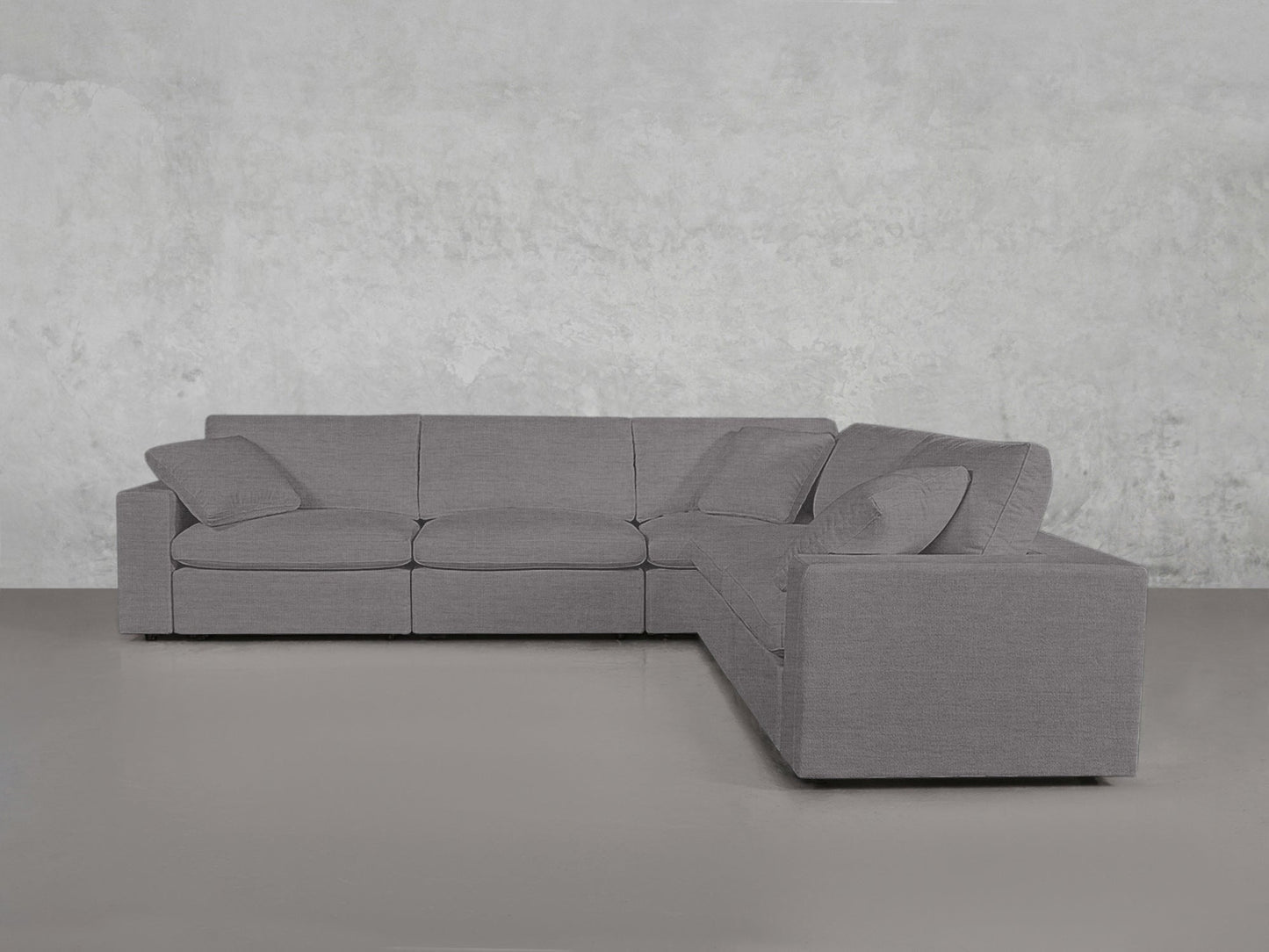 A 5-Seat Modular Corner Sectional in modern gray with four seat cushions and matching back pillows, placed against a plain light gray wall and floor.