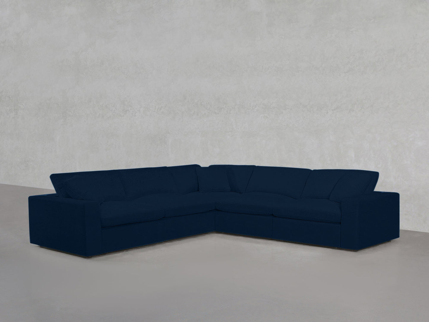 A 5-Seat Modular Corner Sectional in dark blue is set in an empty room featuring light gray walls and a gray floor.