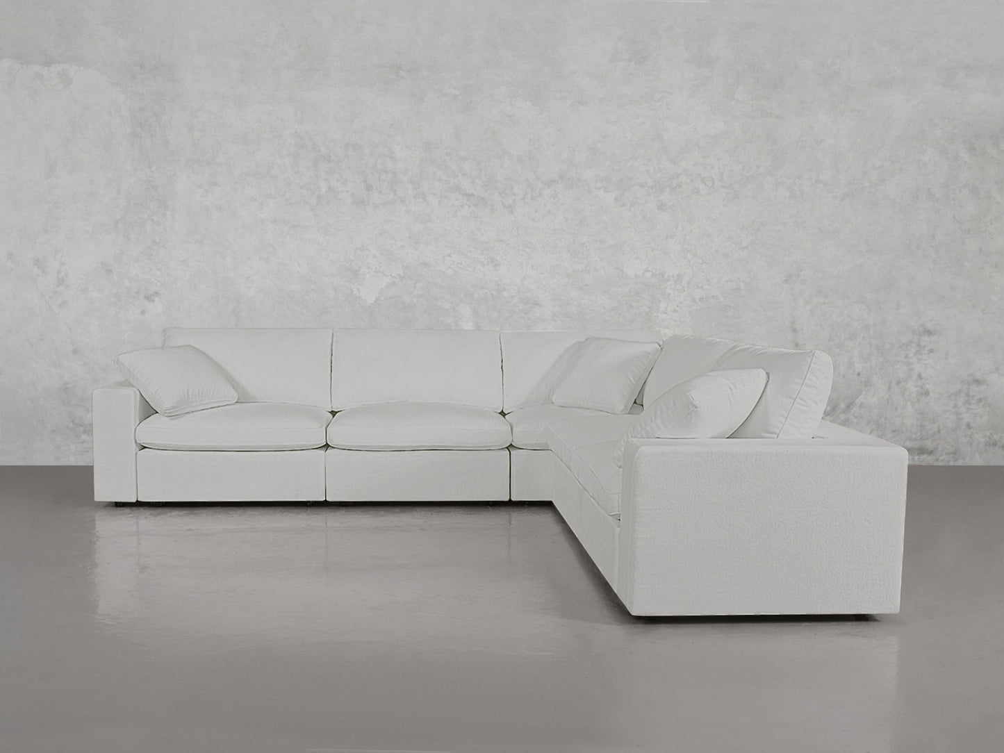 A 5-Seat Modular Corner Sectional in modern white with matching pillows sits on a gray floor against a light textured wall.