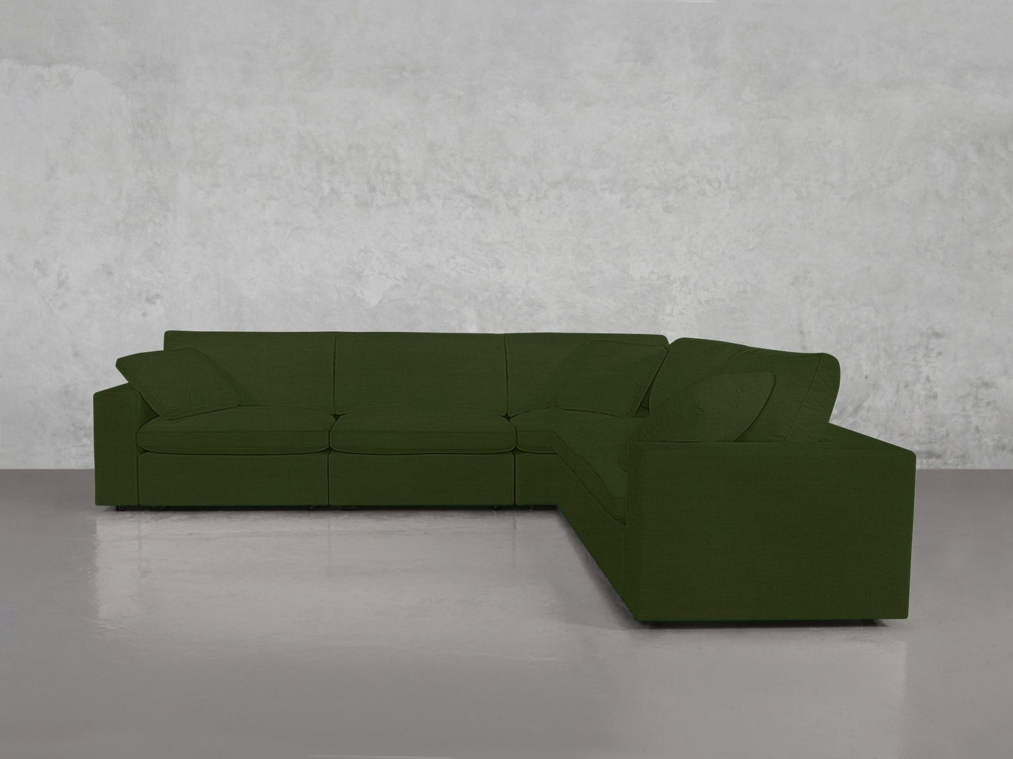 A 5-Seat Modular Corner Sectional in dark green with large cushions sits against a light gray wall on a shiny floor.
