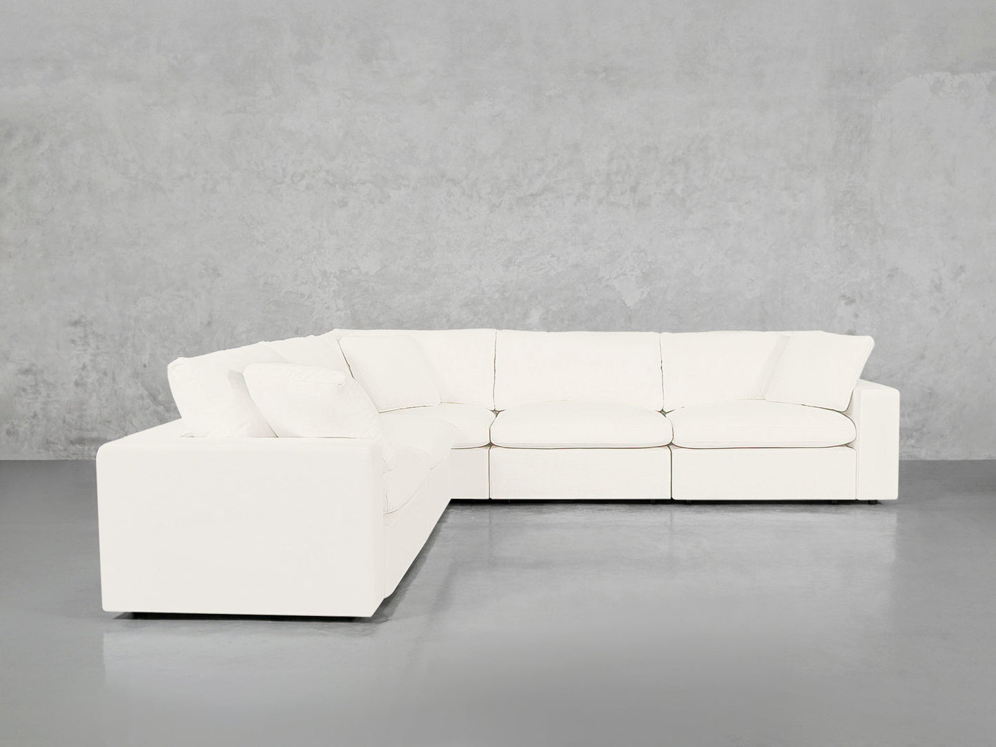The 5-Seat Modular Corner Sectional, in a modern white design with thick cushions and armrests, is set against a plain light gray wall and floor.