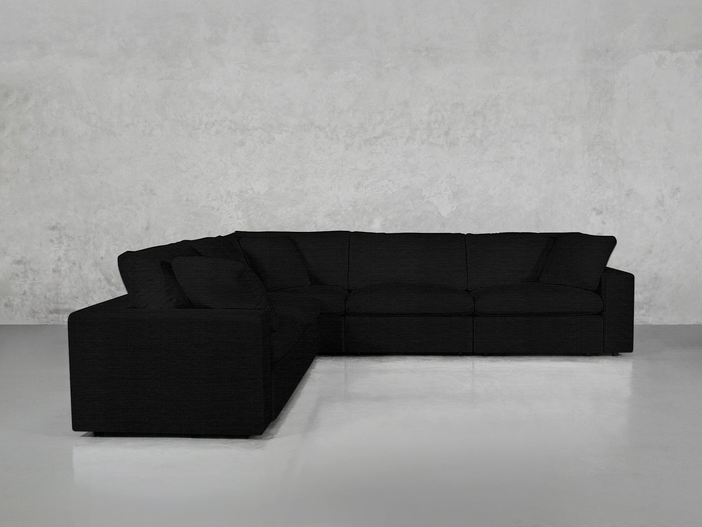 A 5-Seat Modular Corner Sectional in black with plush cushions is set in a modern, empty room featuring light gray walls and a glossy white floor.