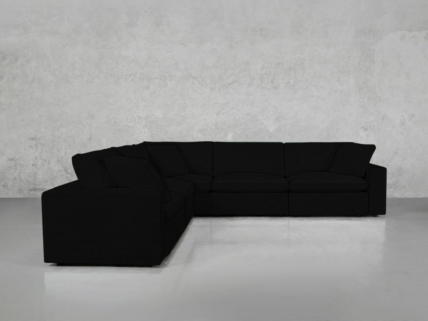 A 5-Seat Modular Corner Sectional with wide cushions and armrests sits in an empty, minimalist room with plain light grey walls and a glossy floor.