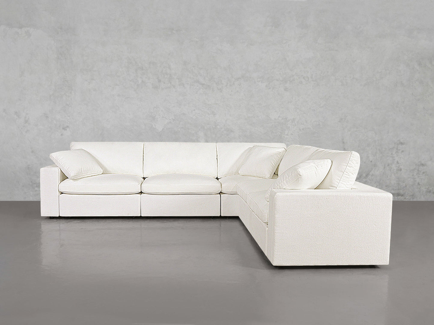 The 5-Seat Modular Corner Sectional, featuring clean lines and matching cushions, is set against a plain light grey wall and a smooth grey floor.