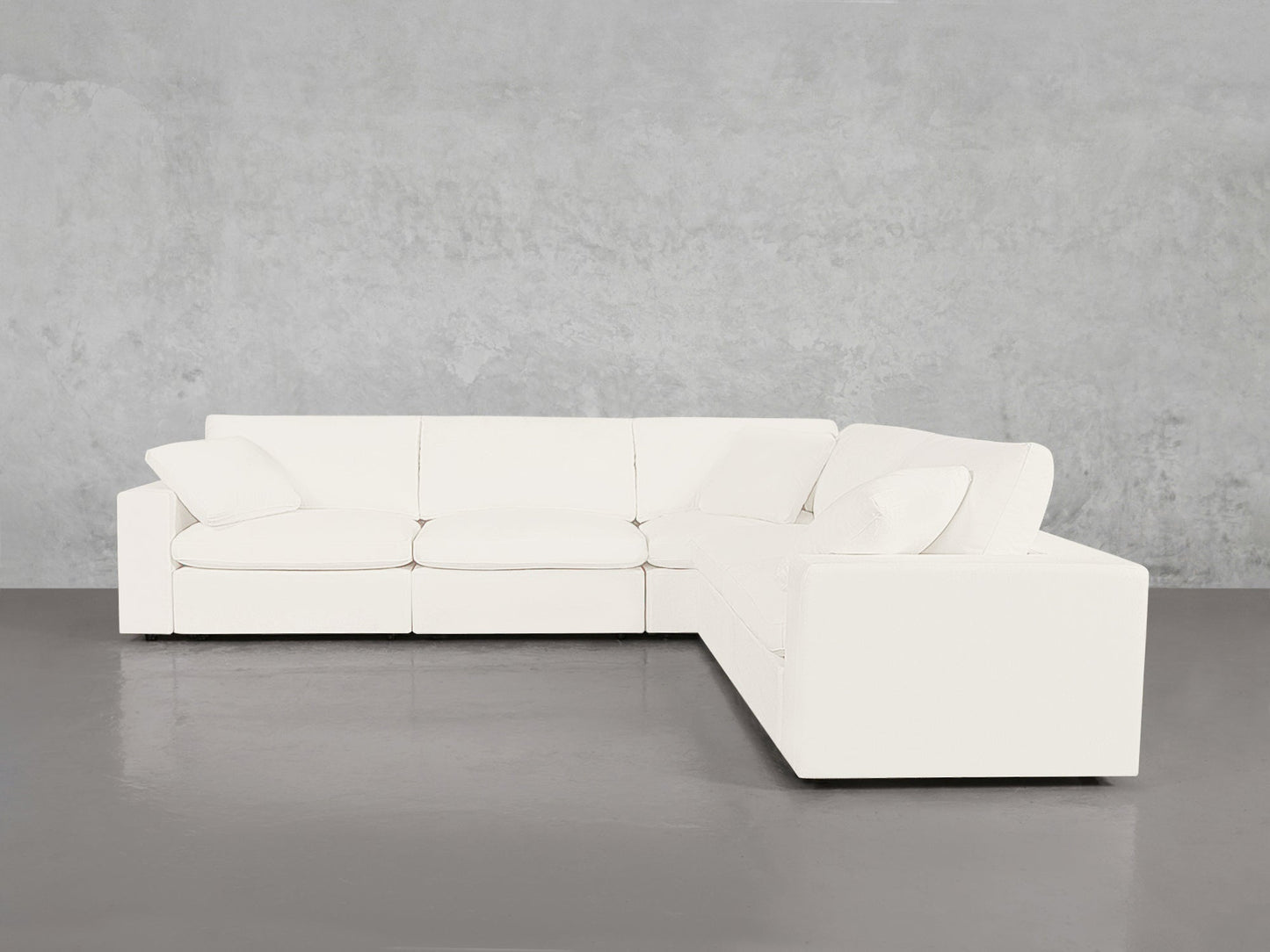 A 5-Seat Modular Corner Sectional with cushions is set against a light gray concrete wall on a polished gray floor.