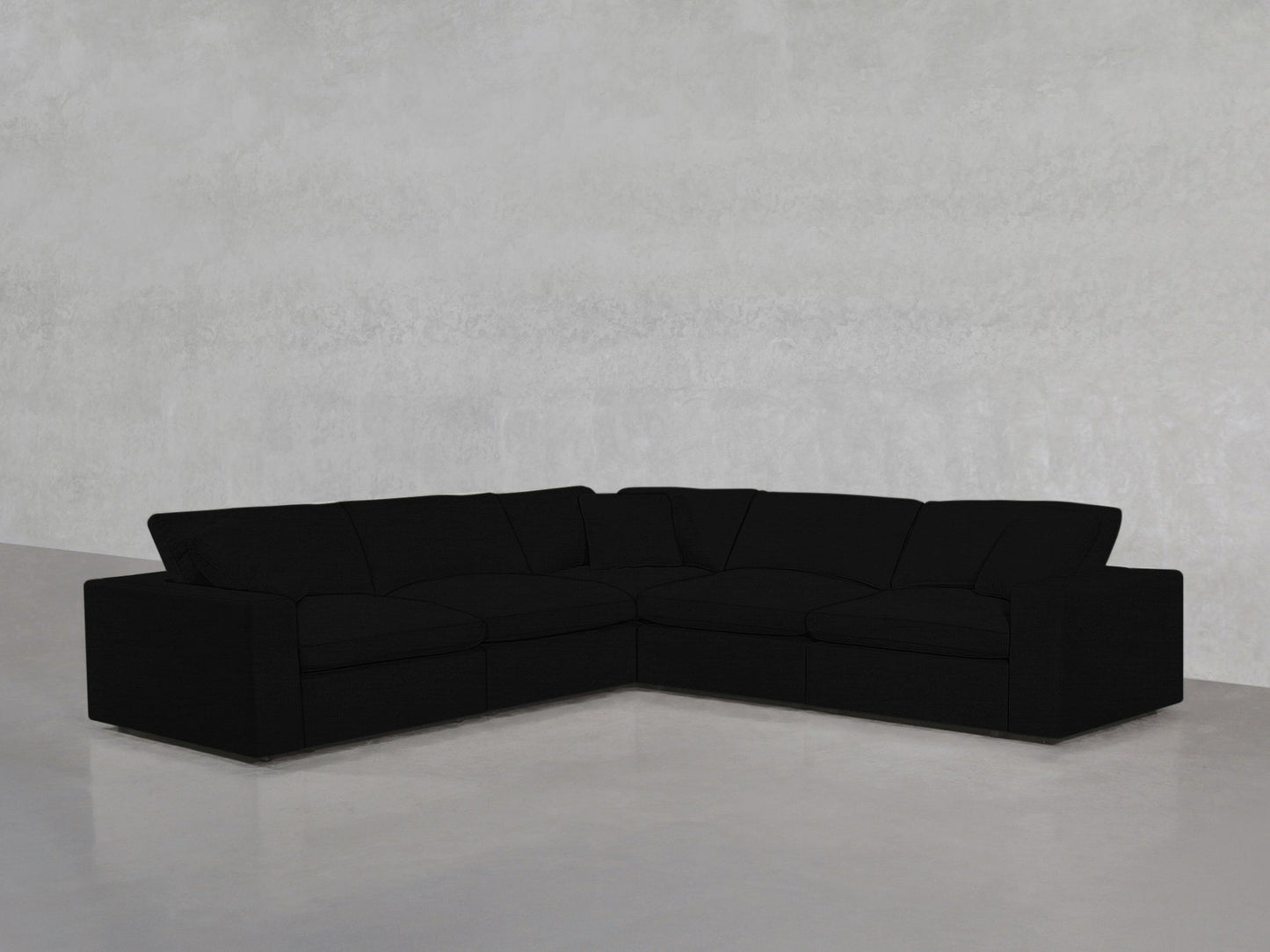 A 5-Seat Modular Corner Sectional with a modern black design and clean lines sits in an empty room featuring light gray walls and a polished concrete floor.