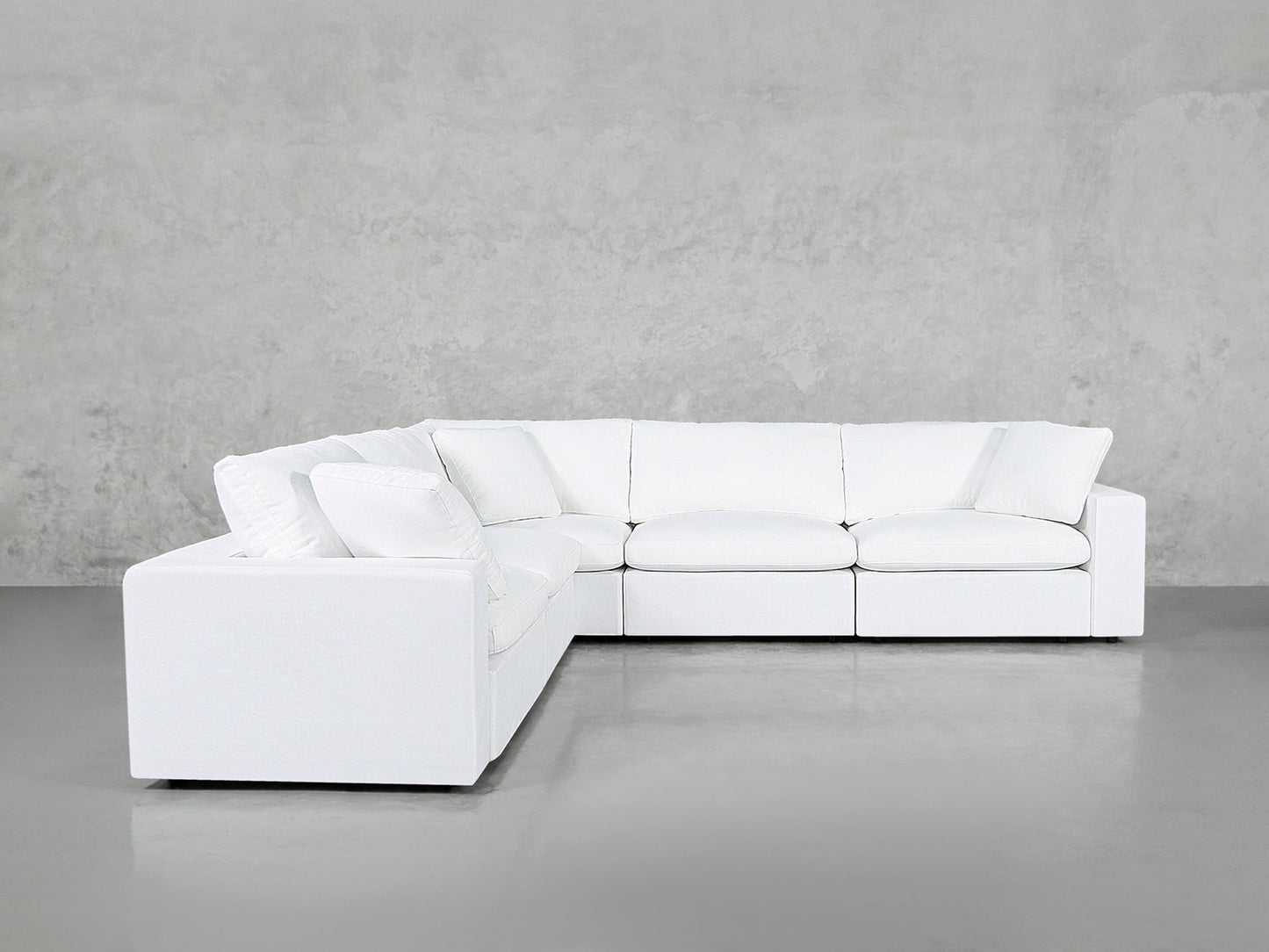 The 5-Seat Modular Corner Sectional with plush cushions sits against a light gray concrete wall and floor, creating a clean, minimalist look.