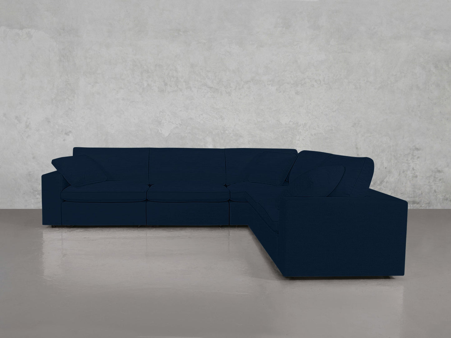 A 5-Seat Modular Corner Sectional with cushions and armrests in dark blue sits on a polished concrete floor against a light gray textured wall.