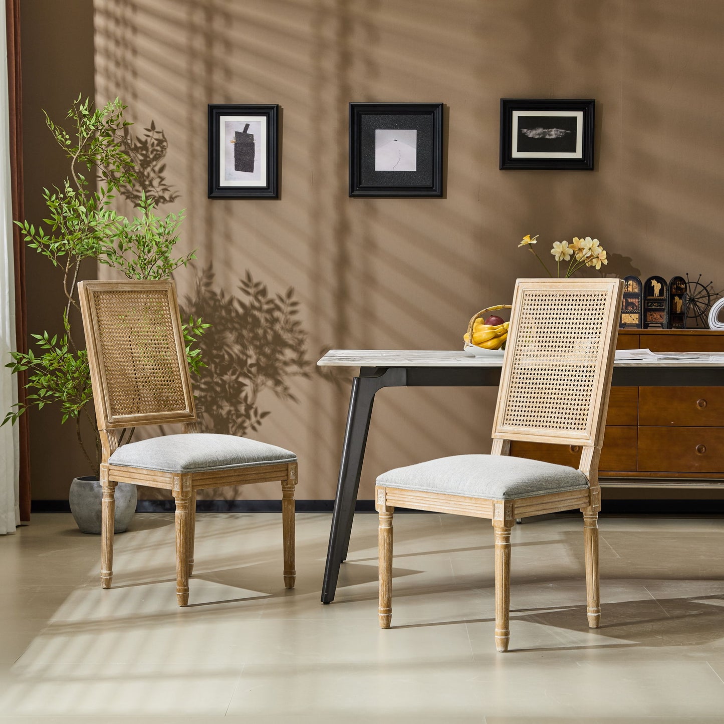 Two French Country Dining Chairs with rectangular cane backrests and smooth upholstered seats sit by a modern table with fruit in a stylish room, complemented by wall art, plants, and a decorated sideboard for a warm, inviting ambiance.