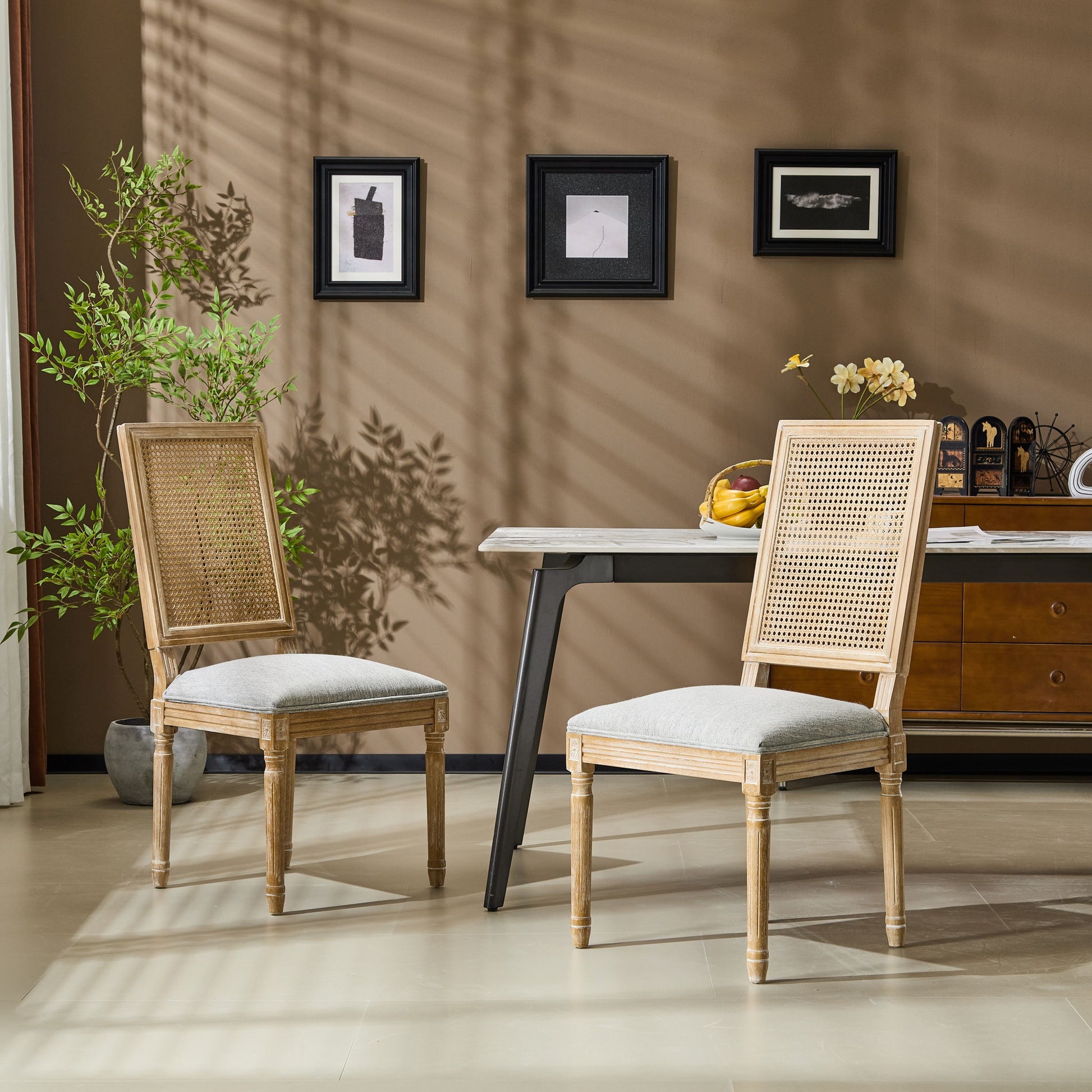 Two French Country Dining Chairs with rectangular cane backrests and smooth upholstered seats sit by a modern table with fruit in a stylish room, complemented by wall art, plants, and a decorated sideboard for a warm, inviting ambiance.
