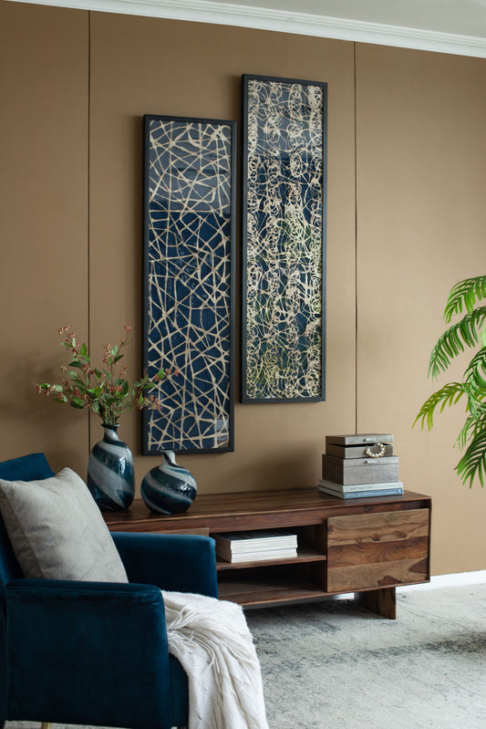 A modern living room with tan walls, two Rectangular Shaped Rice Paper Shadow Box Decor Wall Art (Set of 2) in white/blue, a wooden console table with vases and books, a blue velvet chair, and a leafy green plant in the corner.