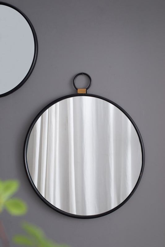 The Wall Mirror With Frame, Contemporary Minimalist Accent Mirror For Living Room, Foyer, Entryway, Bedroom - Black is shown hanging on a gray wall with white curtains reflected. Green leaves and part of another round mirror appear at the edges.