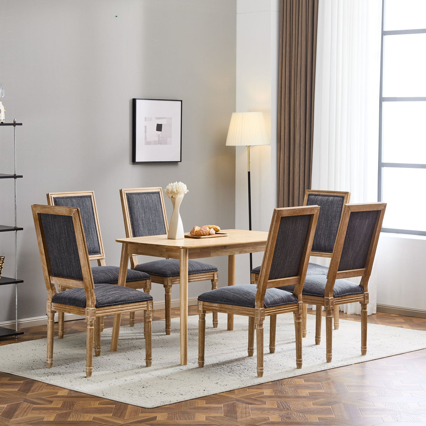 A modern dining room features a wooden table, six French Country Style Dining Chairs with upholstered seating and fluted legs, a floor lamp, artwork on a gray wall, large windows with white curtains, and a vase of flowers on the table.