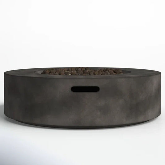 The Fiber Reinforced Outdoor Fire Pit Table in black/gray is a modern round fire pit made of smooth concrete, featuring a central area with small rocks and a rectangular cutout on the side.