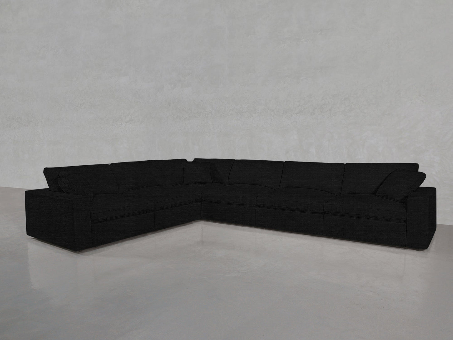 The 6-Seat Modular Corner Sectional in black, with wide armrests and plush cushions, is arranged in an L-shape on a shiny light gray floor against a plain, light-colored wall.