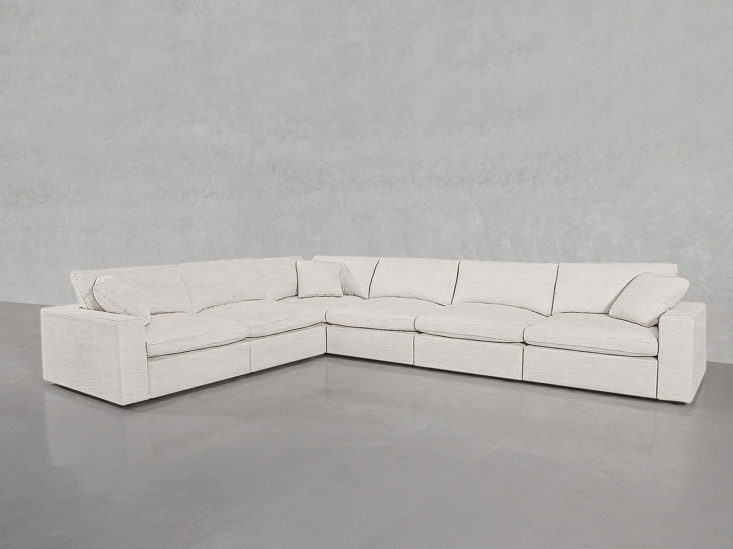 A 6-Seat Modular Corner Sectional, upholstered in light beige fabric, sits on a smooth gray concrete floor against a pale gray textured wall.
