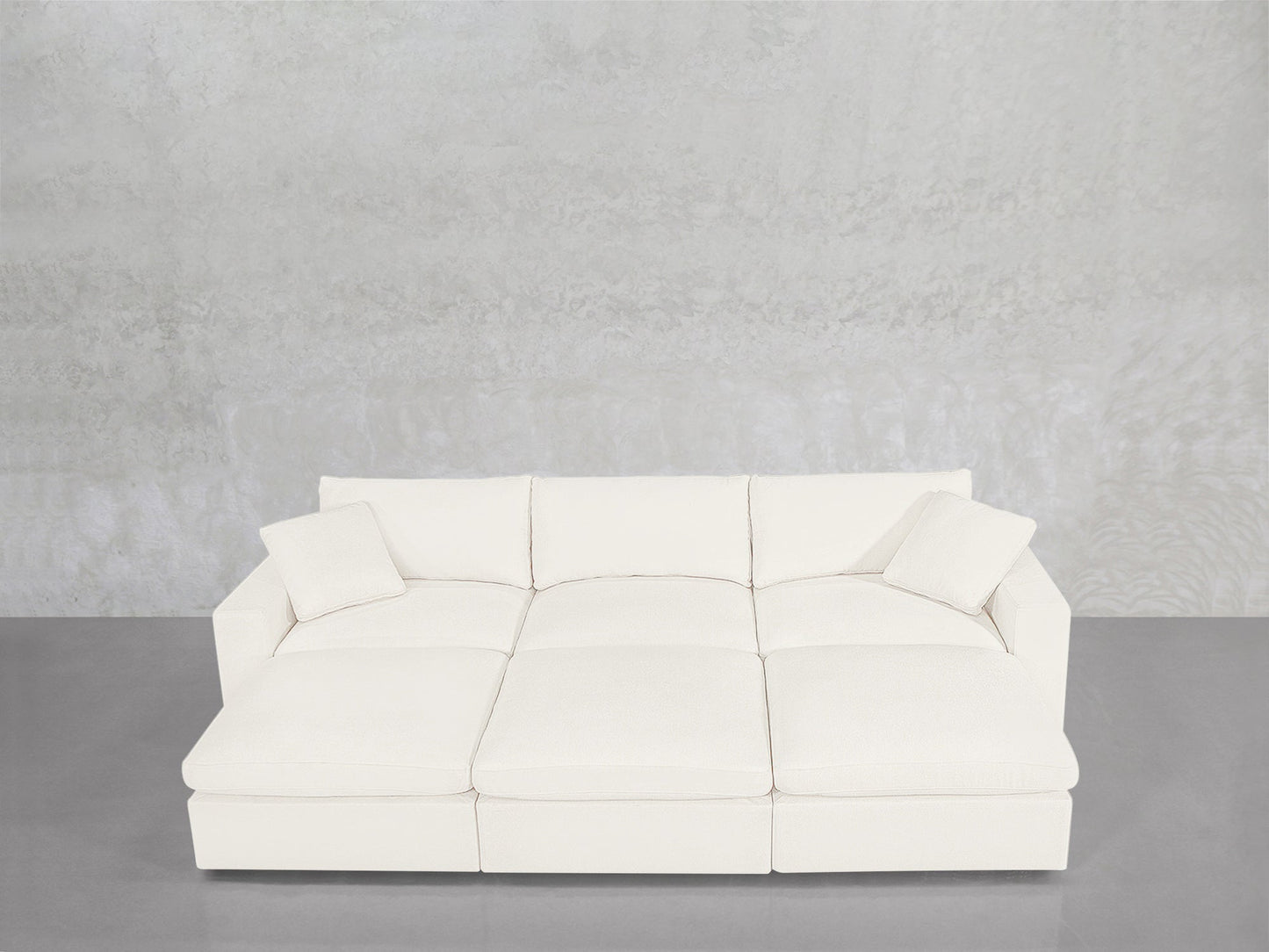 A contemporary 6-Seat Modular Daybed with matching cushions is arranged against a light gray textured wall and a smooth gray floor.