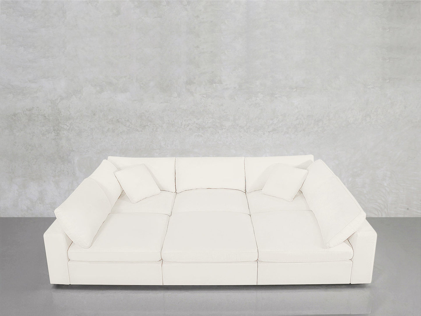A modern white 6-Seat Modular Pit with three seat cushions and four matching pillows sits against a light gray textured wall and glossy gray floor.
