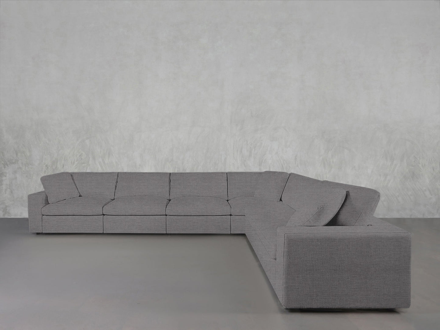 A 6-Seat Modular Corner Sectional in gray rests on a light gray floor beside a textured pale gray wall, offering a minimalist and contemporary interior look.