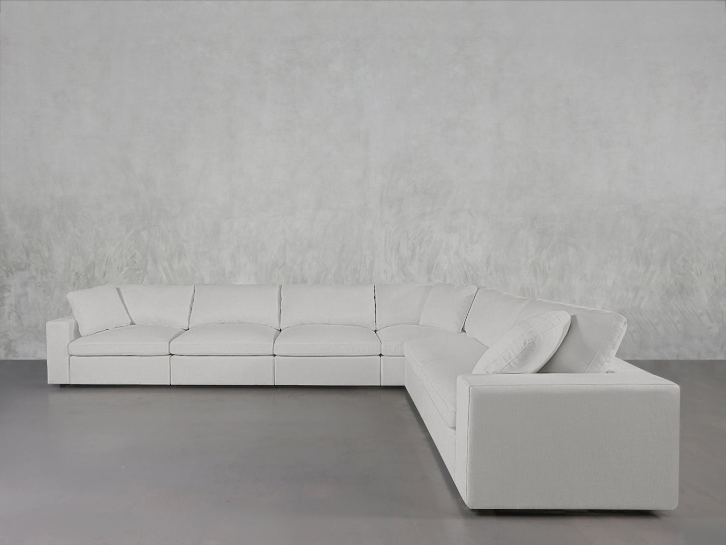 The 6-Seat Modular Corner Sectional, upholstered in light gray fabric, is arranged against a textured pale gray wall on a smooth gray floor.