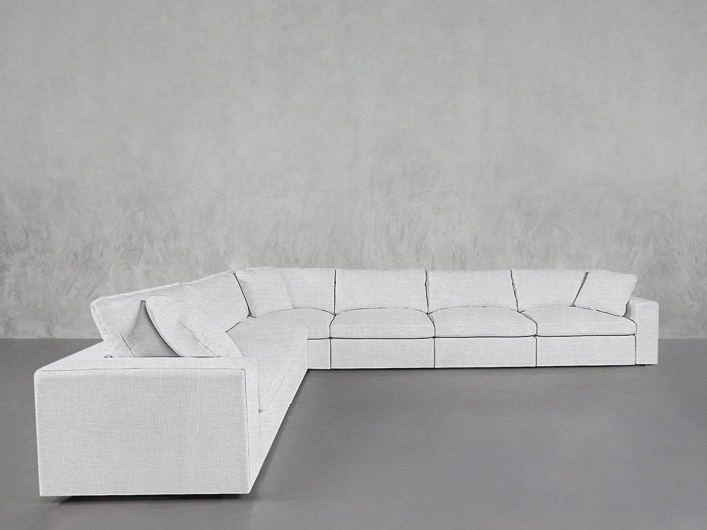 The 6-Seat Modular Corner Sectional, a modern, light gray sofa with clean lines and firm cushions, is arranged in an L-shape against a minimalist, textured gray wall and floor.