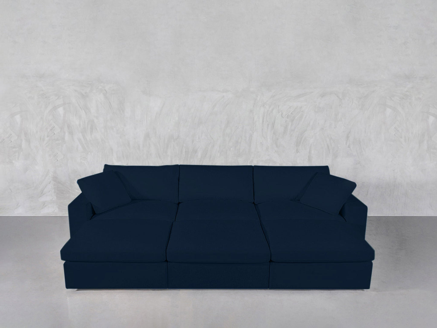 A modern 6-Seat Modular Daybed in dark blue, featuring three seat cushions and four back cushions, is set against a textured light gray wall and placed on a smooth light gray floor.