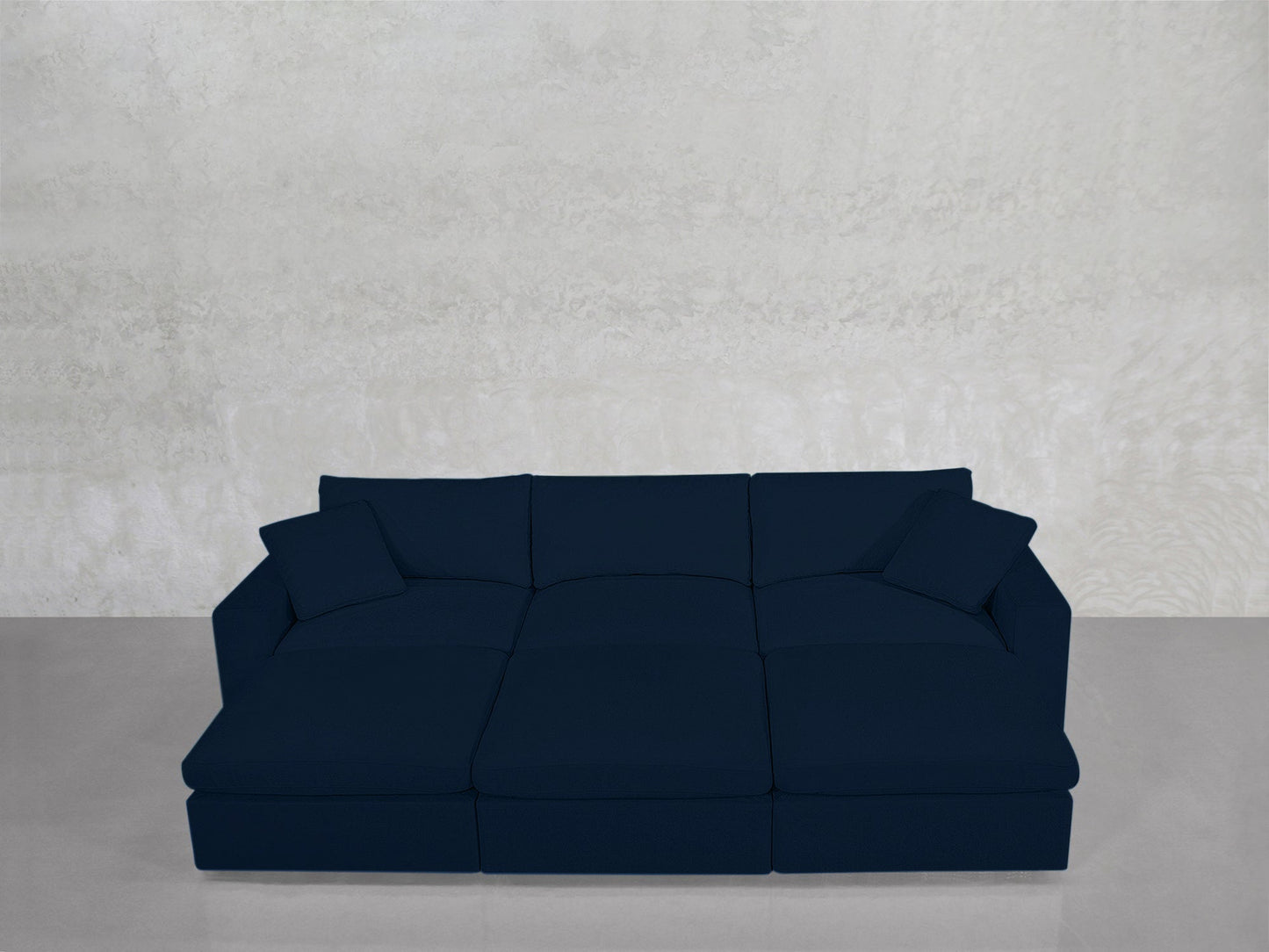 A spacious, dark blue 6-Seat Modular Daybed with two matching cushions rests on a light gray floor against a textured light gray wall.