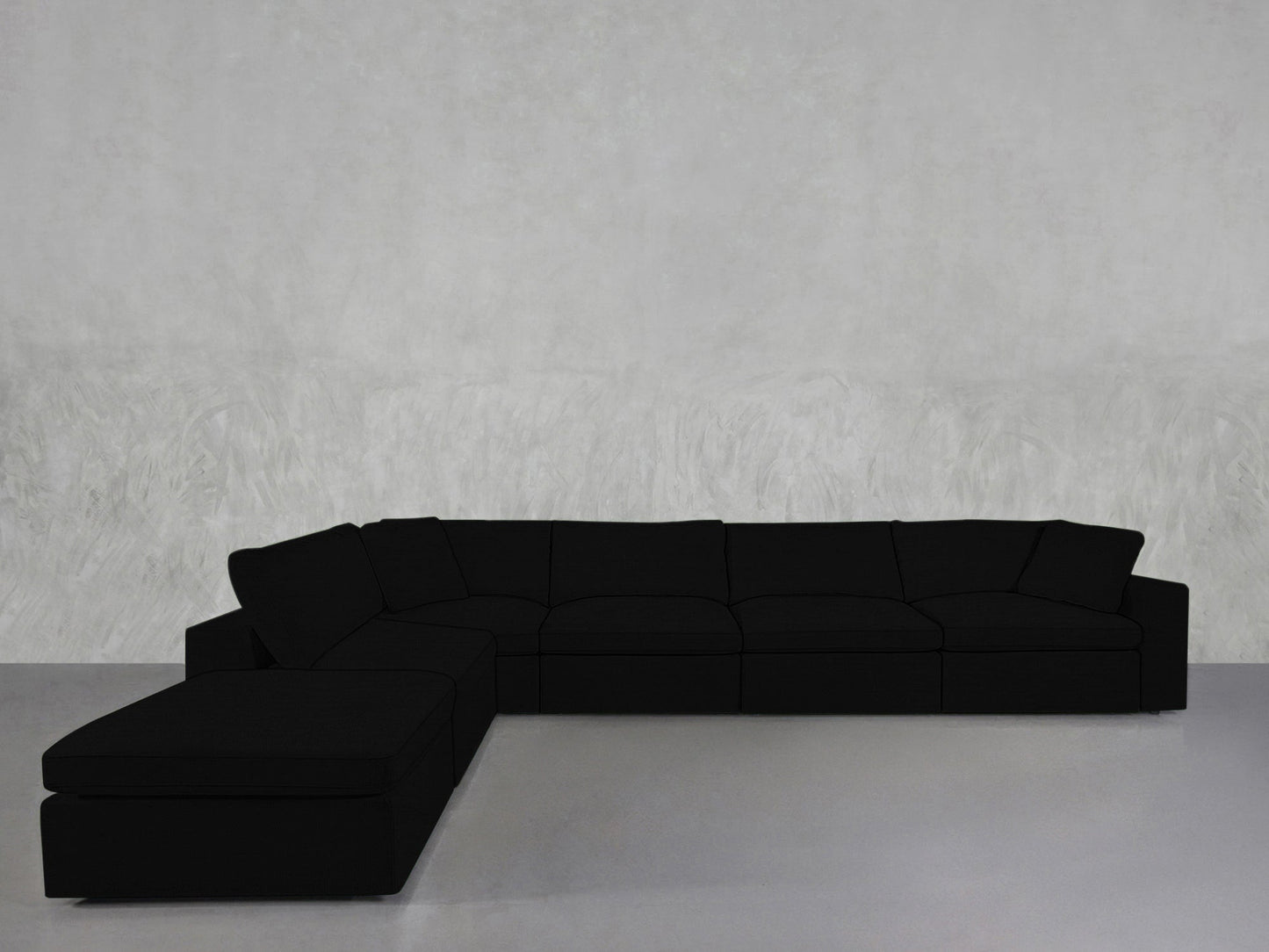 A 6-Seat Modular Corner Lounger Sectional in black is set against a plain, light grey textured wall on a smooth, light-toned floor.